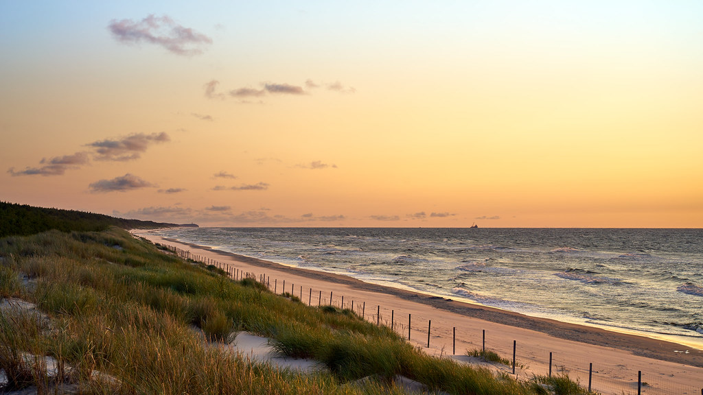 Praia ao entardecer na golden hour, com o céu dourado sobre o mar.