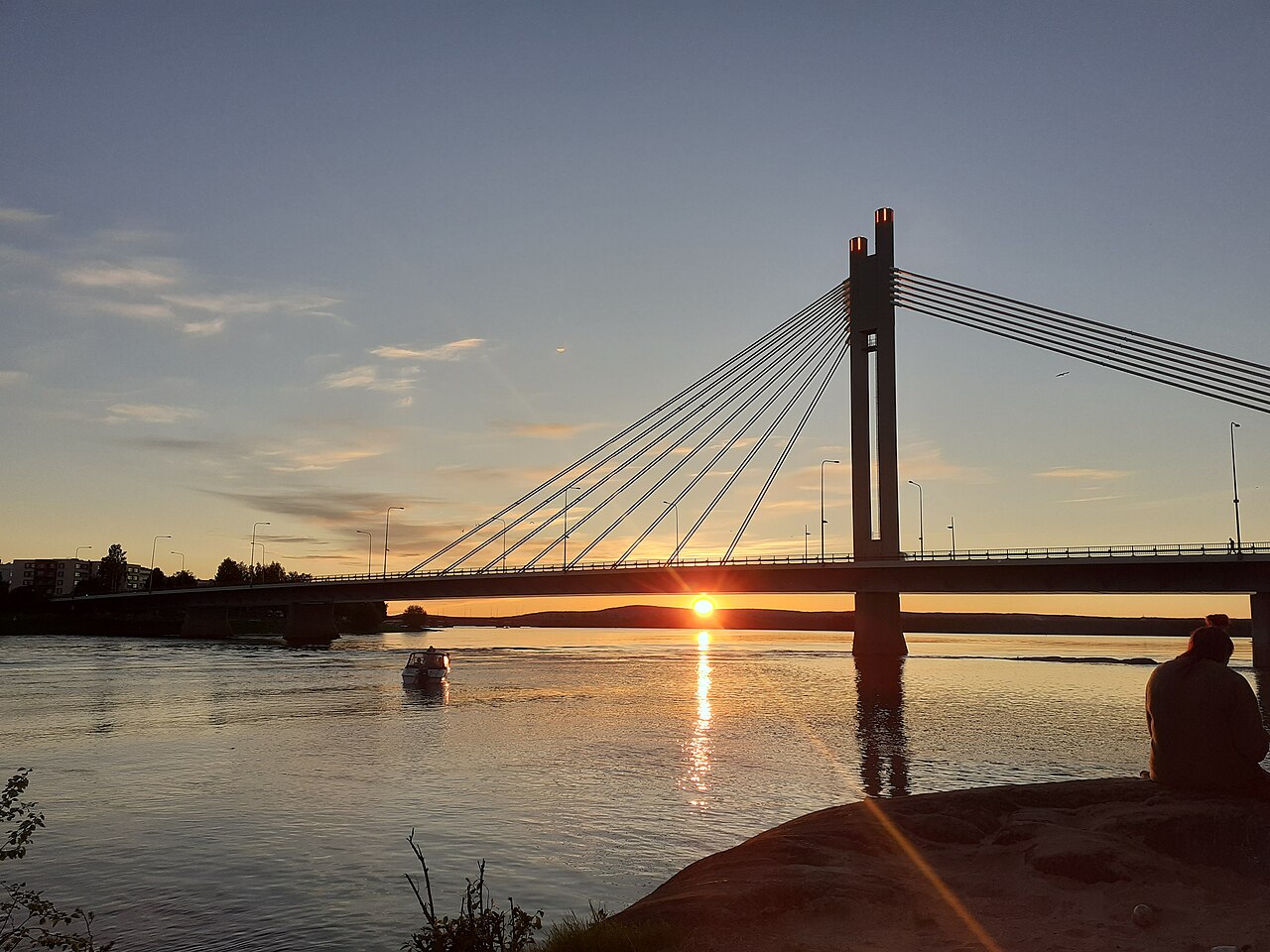 Sol da meia-noite baixo no horizonte sobre um rio, ao lado de uma ponte na Lapônia.