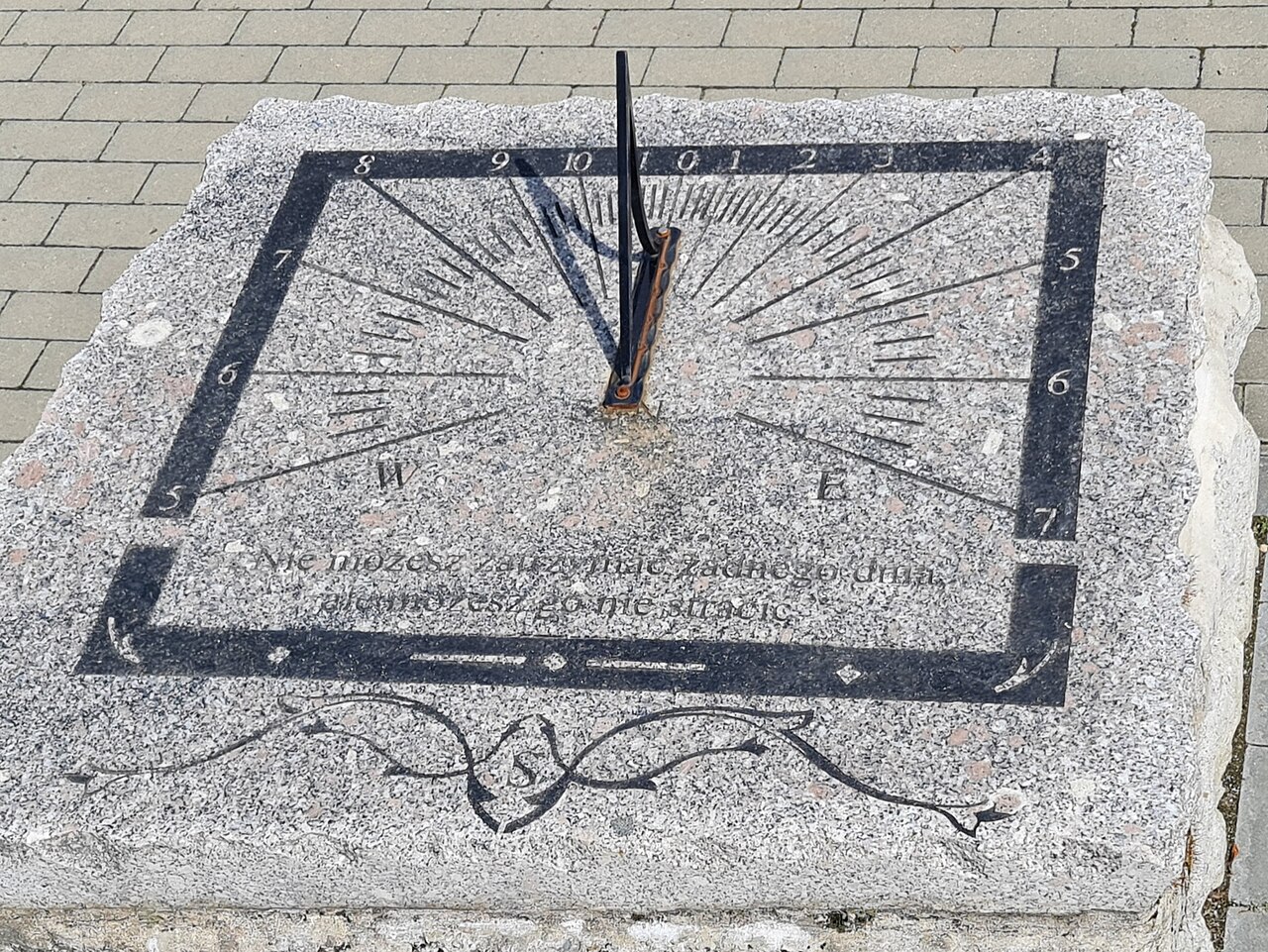 Relógio de sol horizontal com gônomon inclinado projetando sombra sobre o mostrador de linhas horárias.