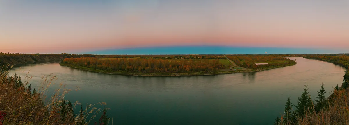 Panorâmica de um rio ao crepúsculo com uma faixa azul escura junto ao horizonte e uma faixa rosa logo acima dela.