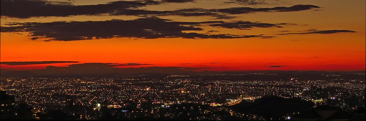 Belo Horizonte vista de cima no fim da tarde, com o céu ainda vermelho e as luzes da cidade já acesas.